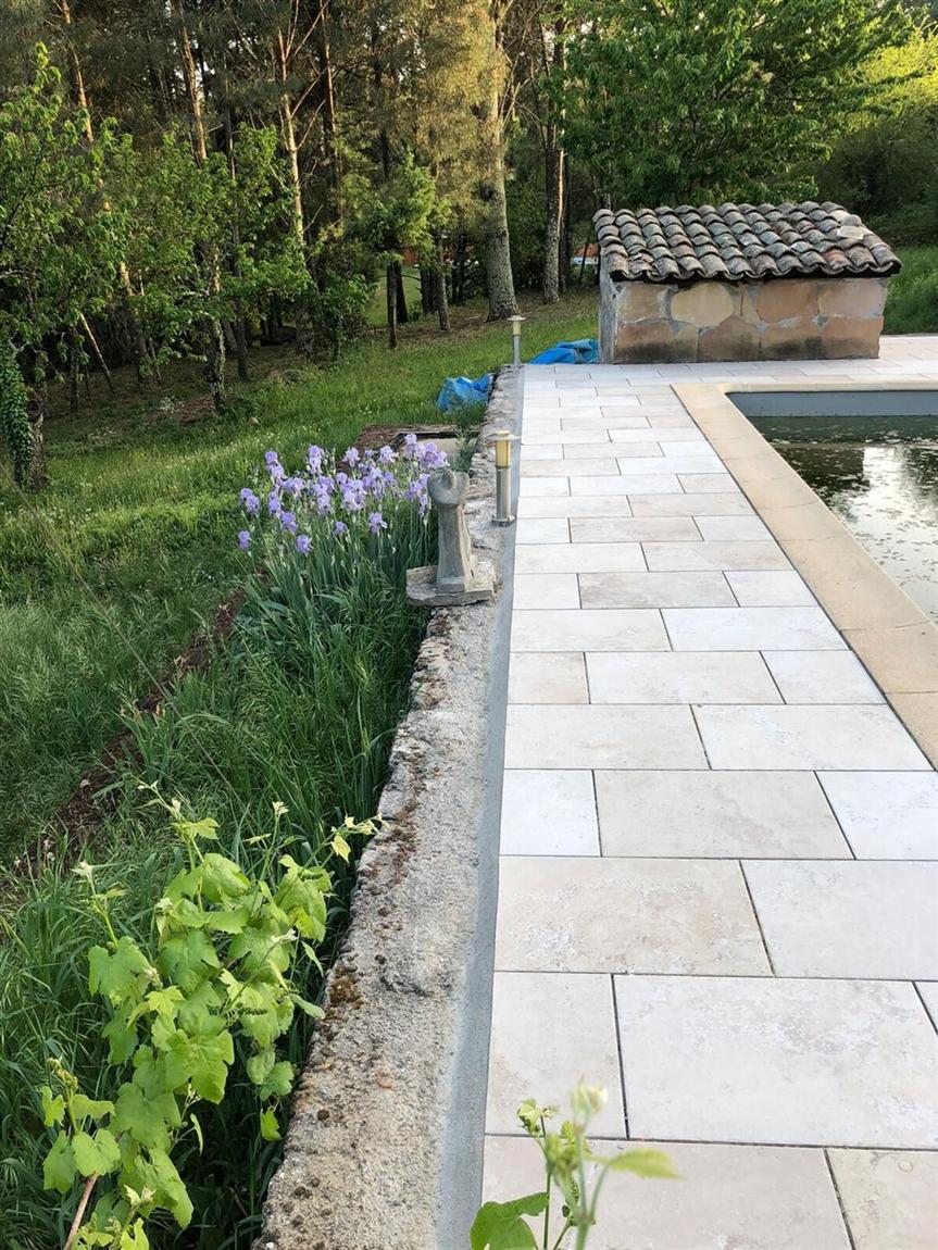 Terrasse en dalles claires bordée de lavandes, au bord d'une piscine
