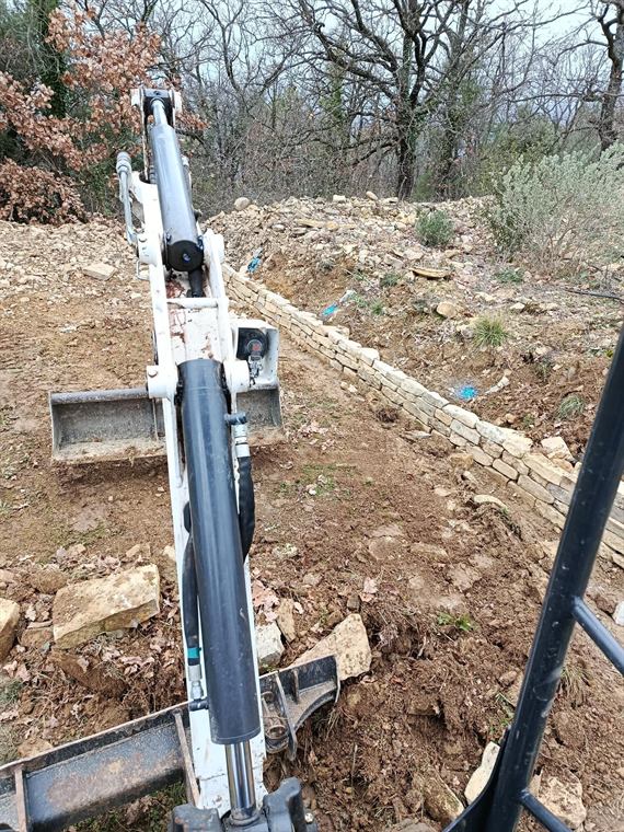 Terrassement au bras de mini-pelle au pied d'un muret
